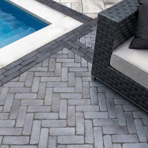 Poolside patio with modern black tiled furniture and grey brick flooring.