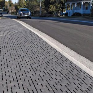 Street sidewalk with textured paving and a car in the background.