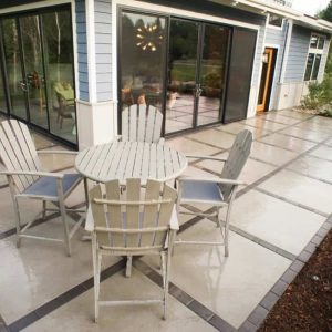 Outdoor patio with round table and chairs in front of a modern house.