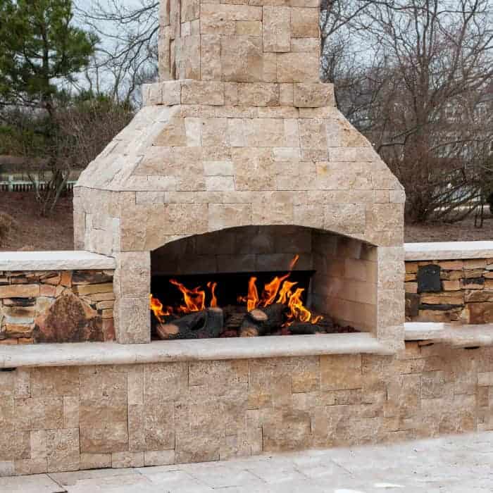 Outdoor stone fireplace with fire burning, ideal for garden and patio gatherings.