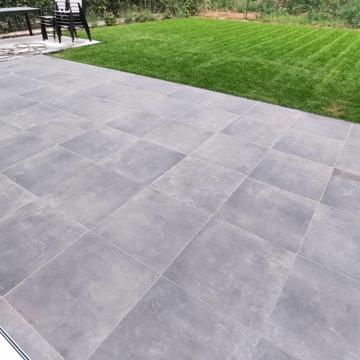 Gray stone patio with lush green grass in backyard.