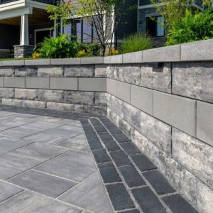 Modern stone wall with landscaping and paving in front of a house.