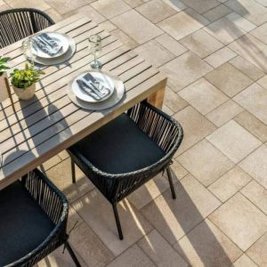 Outdoor dining table with black chairs, plates, and glassware on a tiled patio.