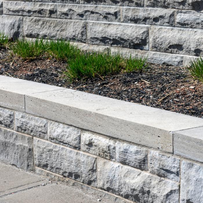 Stone garden bed with green plants and brick wall background.