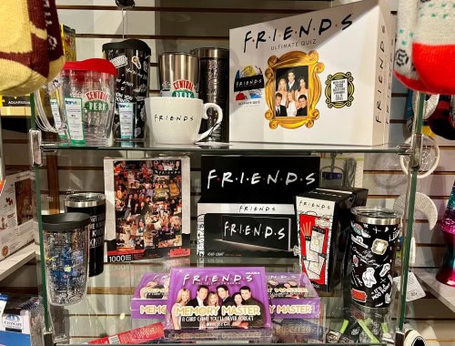 Friends-themed mugs, puzzles, and memory game on glass shelf.