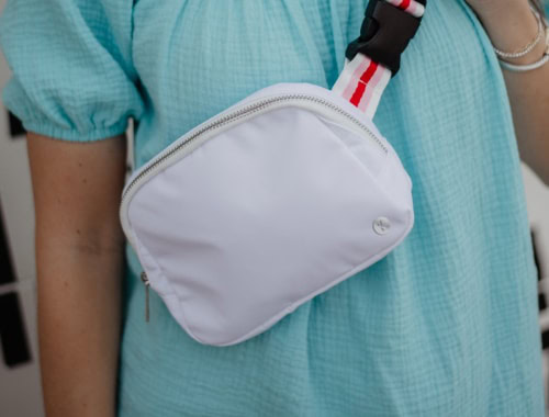 White crossbody bag with red and black strap on a person in a blue dress.