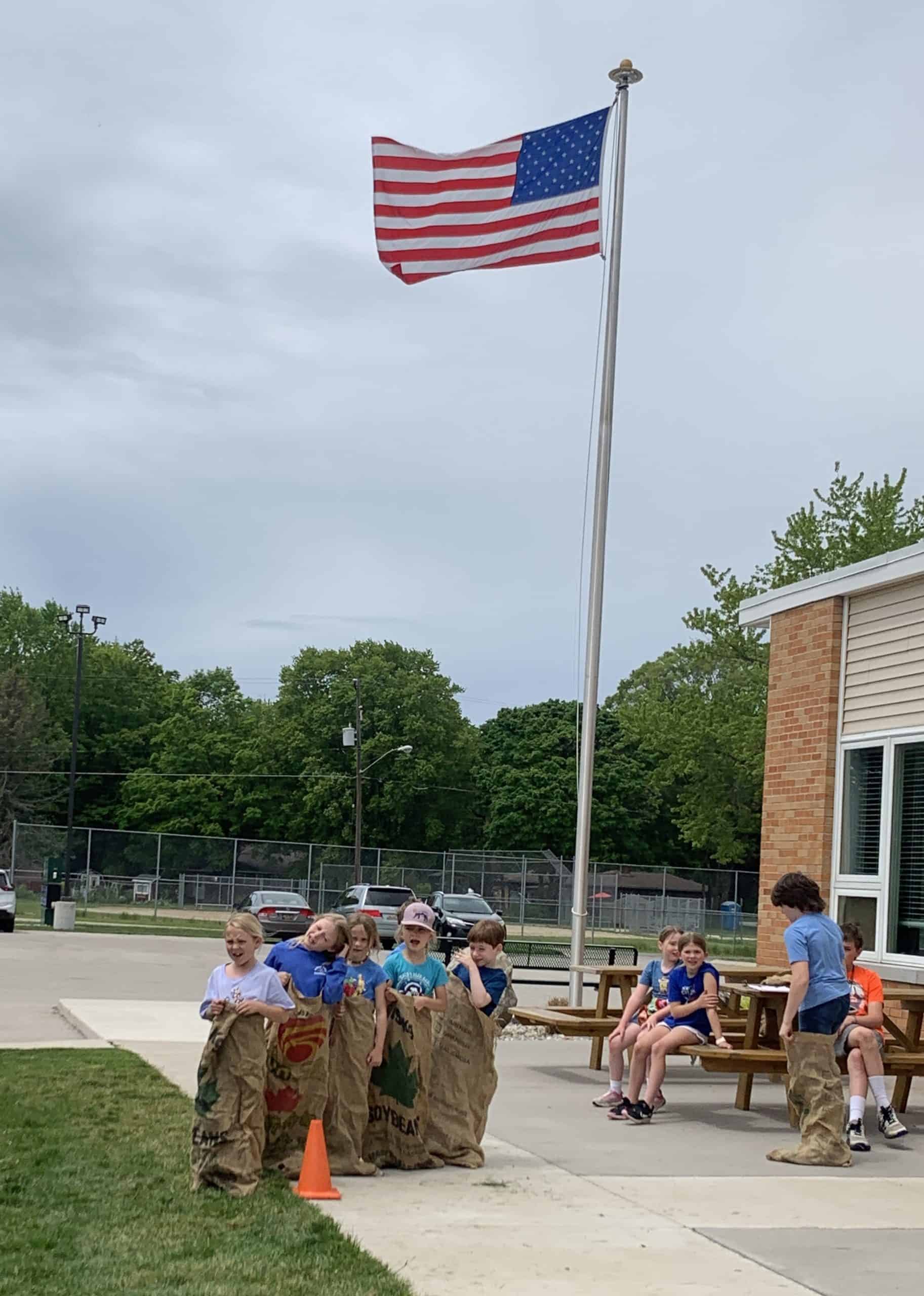Students participating in outdoor activity at New Era Christian School with American flag.