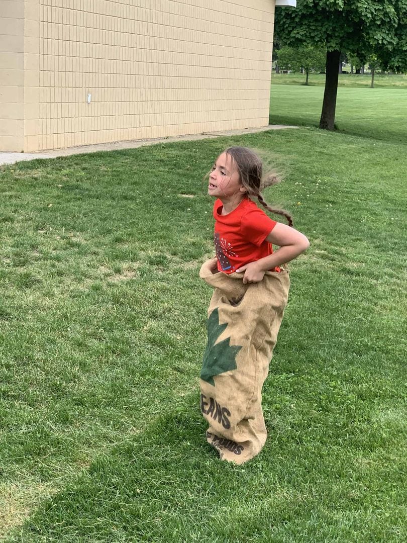 Young girl playing sack race outdoors on green grass.