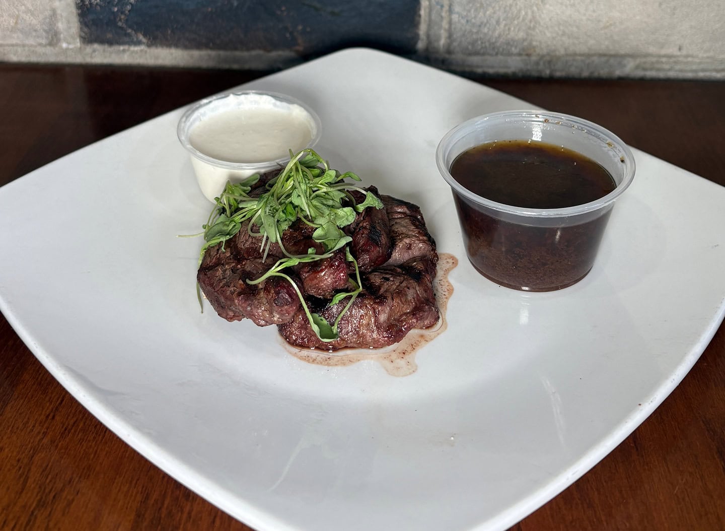 Filet medallions served with creamy sauce, dark gravy, and fresh greens on a white plate.