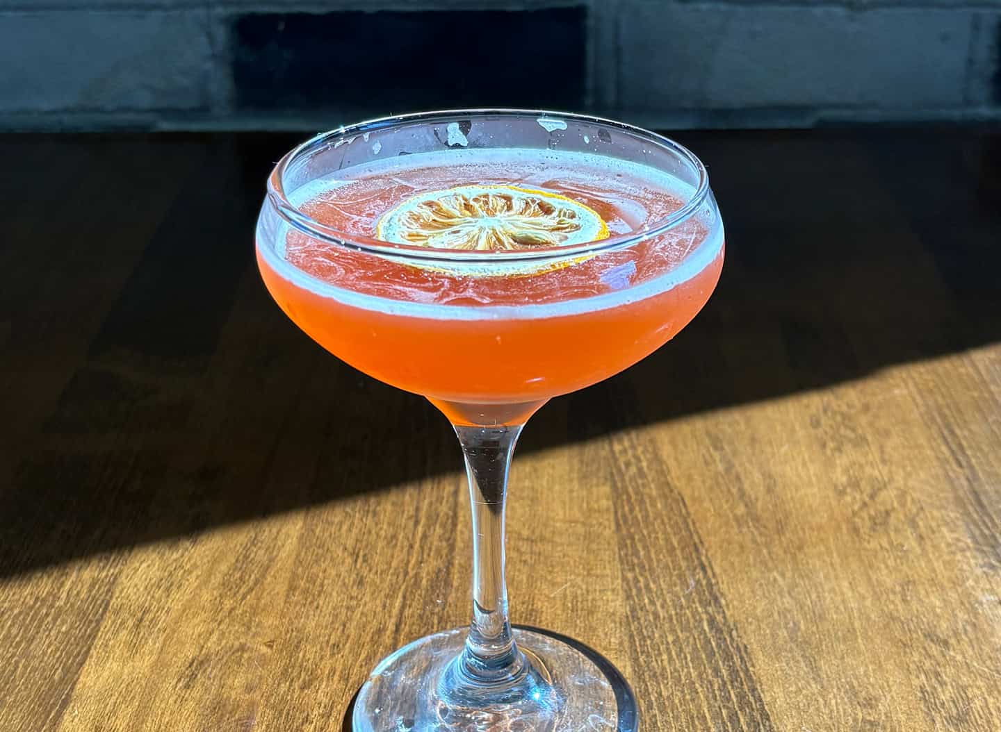 Colorful citrus cocktail with lemon slice in a coupe glass on wooden table.