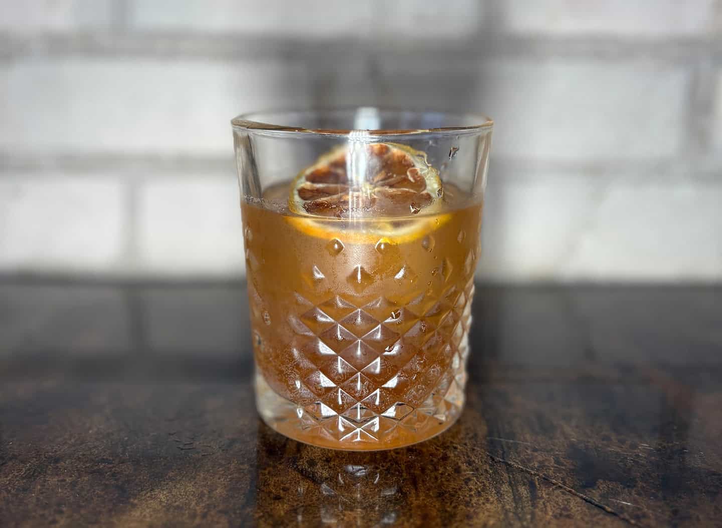 A cocktail with a slice of orange in a textured glass on a wooden surface.