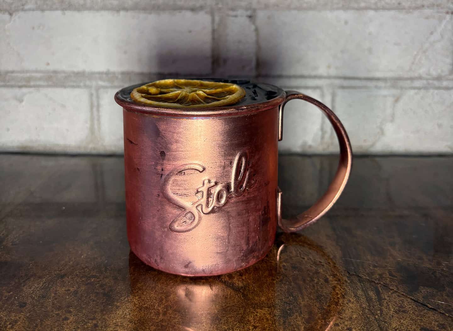 Copper mug with lemon slices and a dark beverage inside.