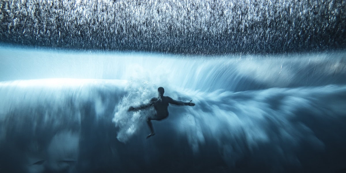 Surfeur plongeant dans une vague majestueuse, explorant les merveilles du monde sous-marin.