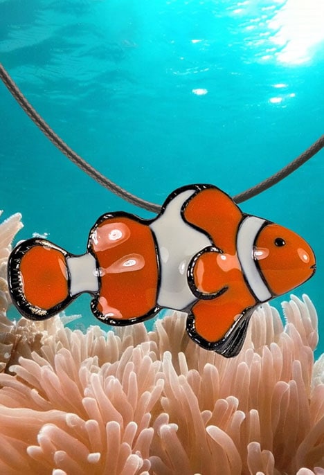 Un pendentif en forme de poisson-clown flotte au-dessus d'une anémone, évoquant l'éclat coloré des récifs coralliens.