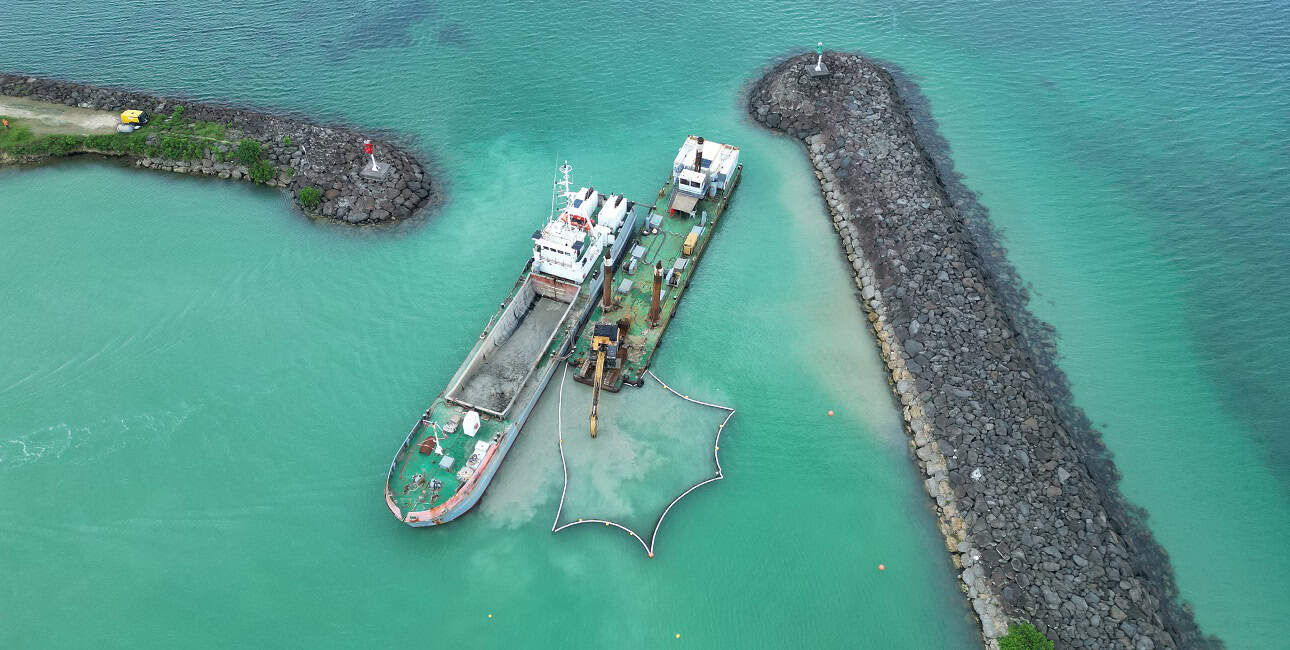 Un navire de dragage opère dans un port entouré de digues rocheuses, illustrant l'importance de l'entretien maritime.
