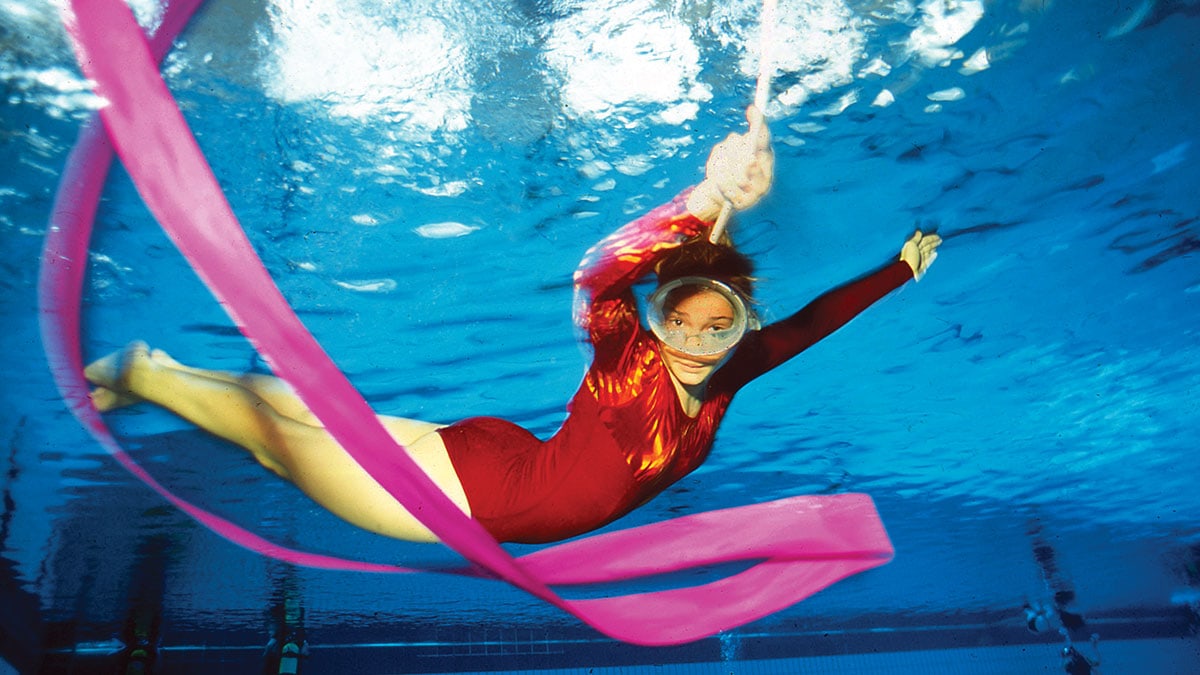 Une nageuse artistique évolue gracieusement sous l'eau, créant des motifs fluides avec un ruban rose, symbole de liberté a...