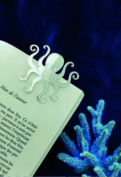 Un marque-page en forme de poulpe évoque l'exploration marine, niché entre les pages d'un livre, sur fond de corail bleu.
