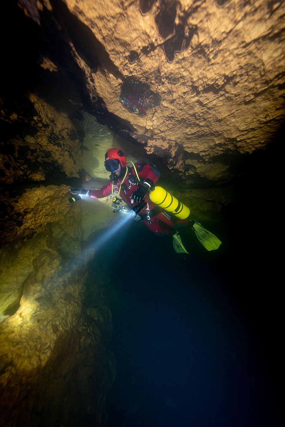 Plongée exploratoire dans une grotte sous-marine, illuminée par une lampe, révélant des formations rocheuses.