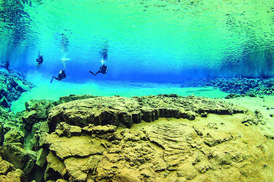 Des plongeurs explorent un paysage sous-marin fascinant avec des formations rocheuses et des eaux cristallines.