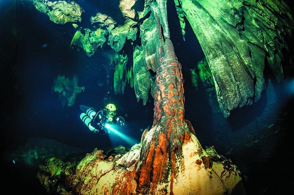 Un plongeur explore une grotte sous-marine ornée de formations rocheuses fascinantes et colorées.