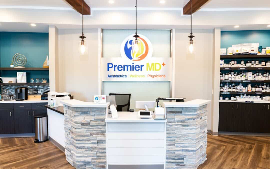 Modern medical clinic reception with PremierMD+ logo and pharmacy shelves.