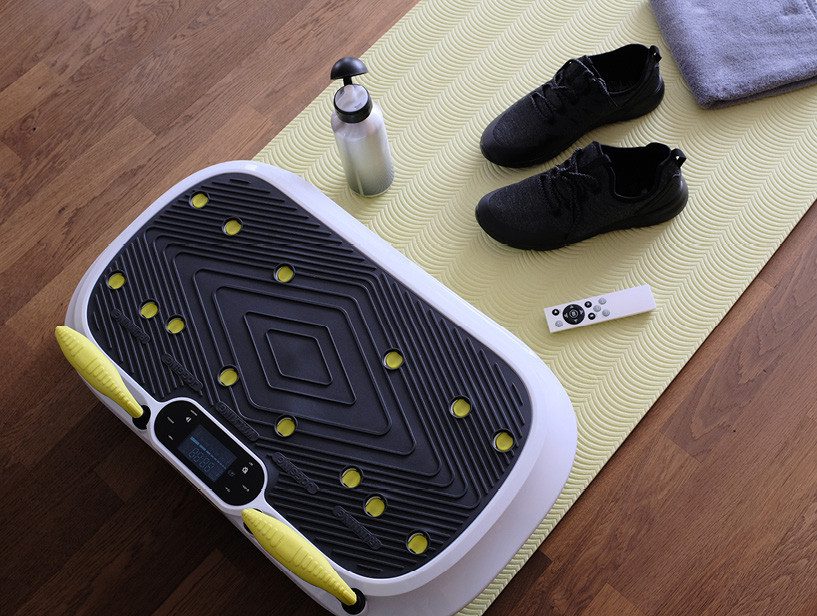 Exercise equipment on yoga mat including balance board, water bottle, shoes, and remote.