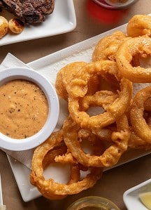 Golden fried onion rings served with dipping sauce at Prime Steakhouse for a delicious appetizer.