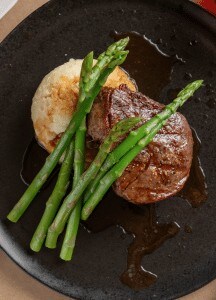 Juicy grilled steak with green beans and mashed potatoes on a black plate.