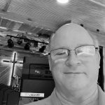 Man with glasses smiling in a modern indoor setting.