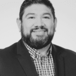 Headshot of Ramon R. in a suit and checkered shirt.