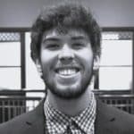 Young man with curly hair and a beard smiling in an indoor setting.