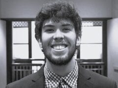 Young man with curly hair and a beard smiling in an indoor setting.