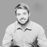 Black and white photo of a smiling man in a collared shirt.
