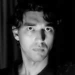 Black and white portrait of a young man with curly hair and intense gaze.