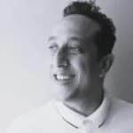 Portrait of a man smiling, in grayscale, with short curly hair.