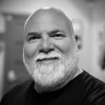 Close-up of a smiling man with a beard in black and white.
