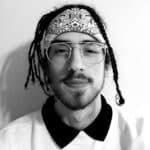 Young man with glasses and bandana, smiling at the camera.