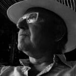 Side profile of a man wearing a hat and glasses in black and white.