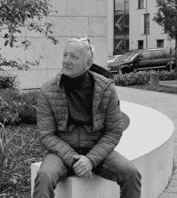 Man sitting on a curved concrete bench outdoors in a park setting.