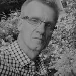 Portrait of Anthony C. with glasses and checkered shirt in outdoor setting.