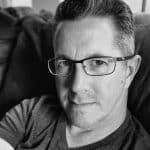 Portrait of a man with glasses, looking at the camera in black and white.