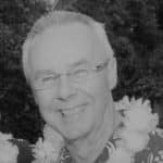 Portrait of a smiling man with glasses and a flower lei outdoors.