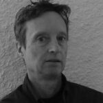 Black and white portrait of a man with short hair against a textured wall.