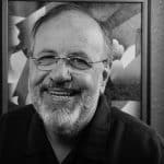 Portrait of Brian G. smiling, wearing glasses, in front of abstract art.