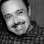 Smiling man with dark hair and beard in black and white.