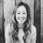 Portrait of a smiling woman with wavy hair in front of a wooden background.
