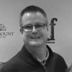 Smiling man wearing glasses in front of a backdrop.