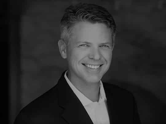 Portrait of Dustin Gardner, smiling, in professional attire.