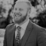 Smiling man in suit outdoors, professional headshot.