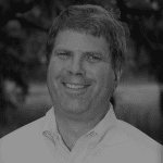 Portrait of Dan S. smiling outdoors in black and white.